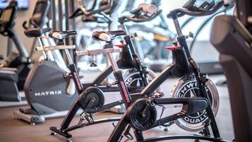 A stationary bike with a digital display and a red seat, positioned in a gym with other exercise equipment.