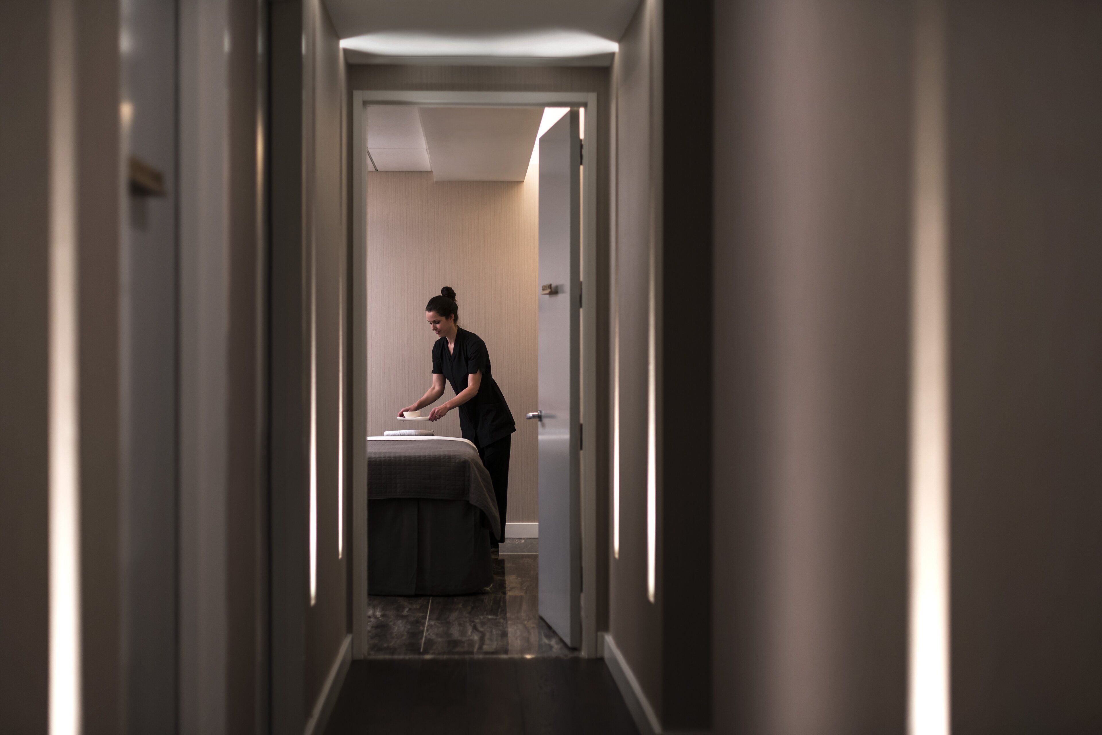 A narrow hallway with a bed and a person attending to it.
