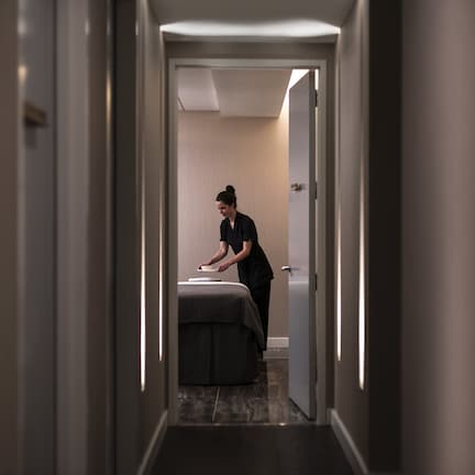 A narrow hallway with a bed and a person attending to it.
