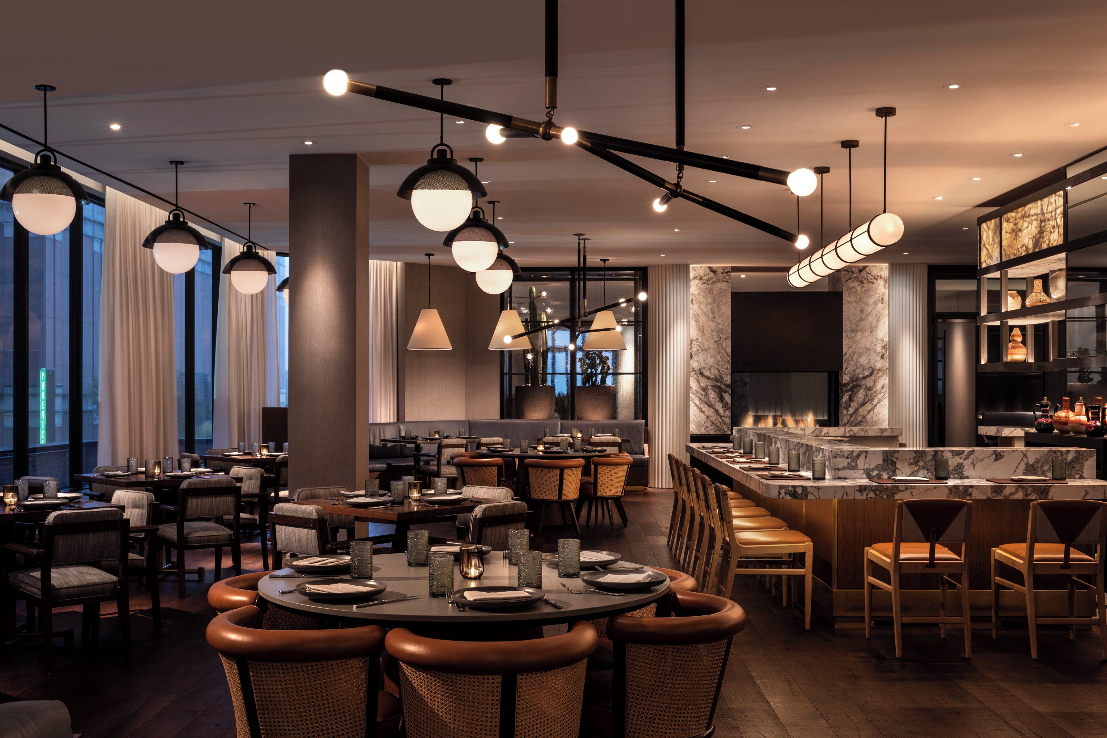 Un restaurante moderno con mesas redondas, asientos de bar e iluminación colgante.