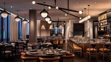Un restaurante moderno con mesas redondas, asientos de bar e iluminación colgante.