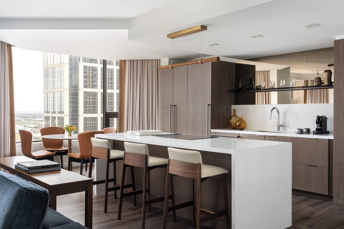 A modern kitchen with a central island, bar stools, and a dining area with chairs.