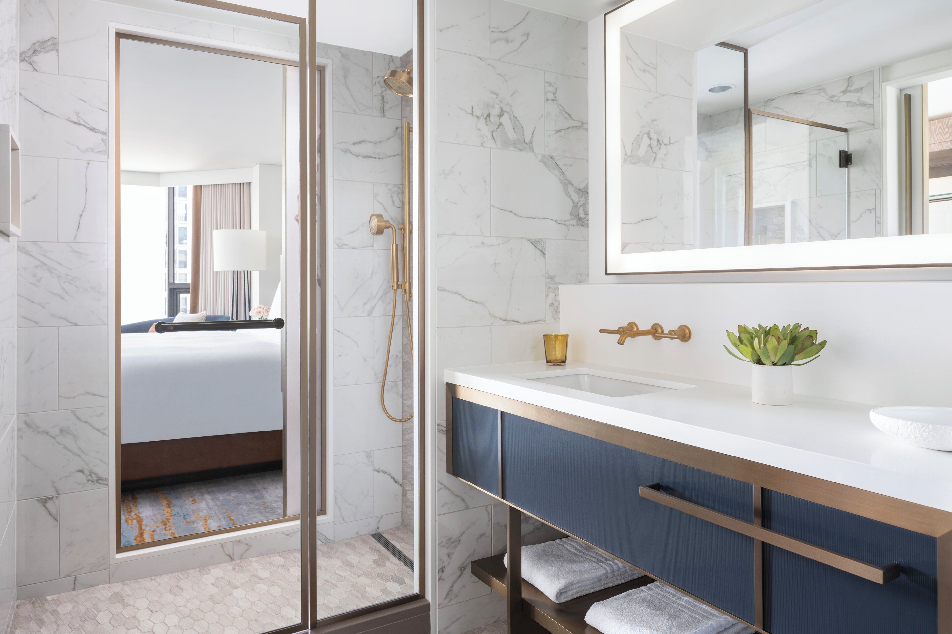 A modern bathroom with a marble floor, a glass shower enclosure, a white sink, and a large mirror.