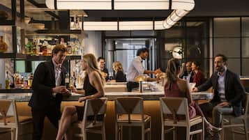 A modern bar area with high stools, a bar counter, and a variety of bottles.
