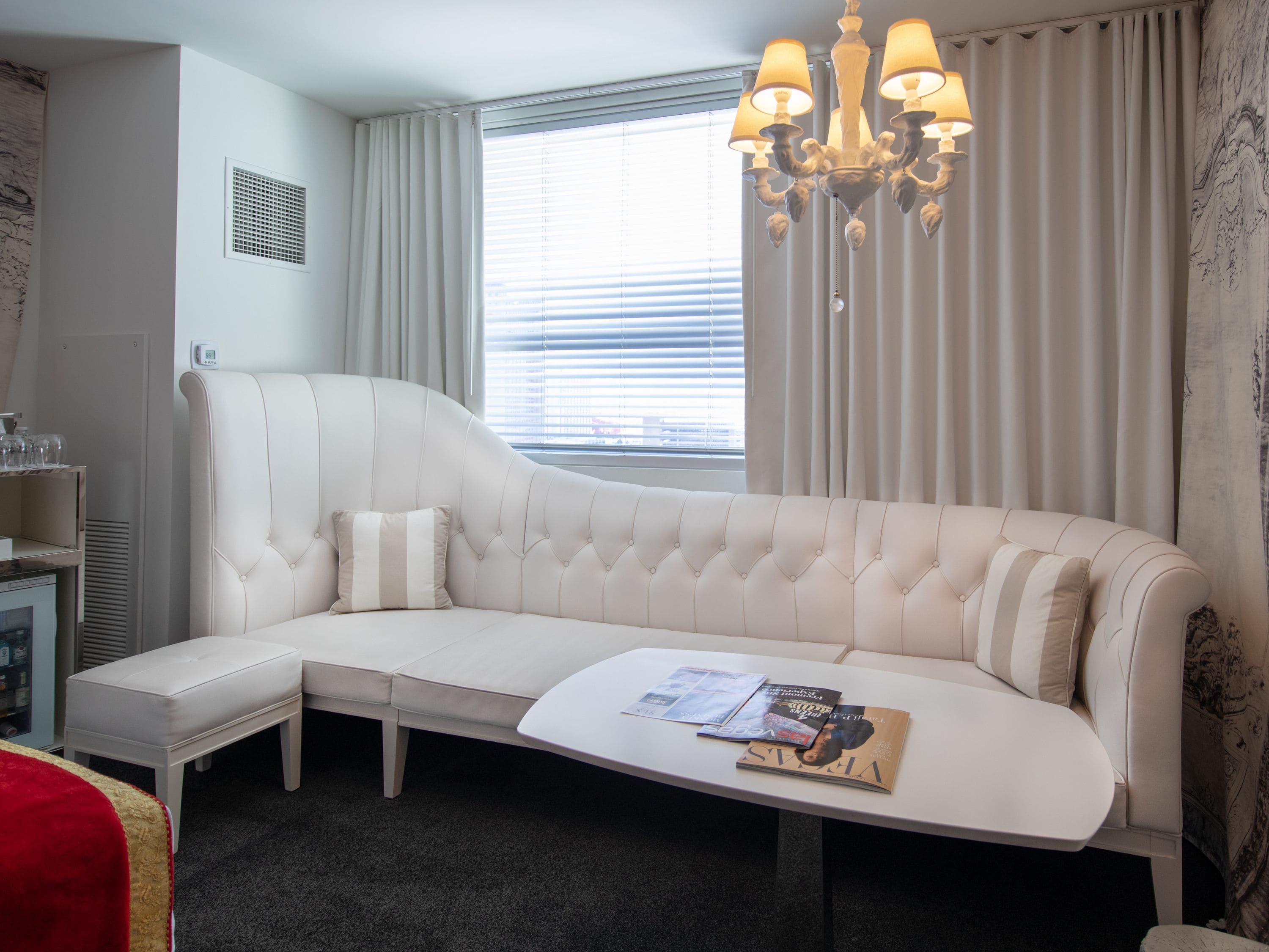Una habitación de hotel moderna con un sofá blanco curvo, una mesita y una araña.