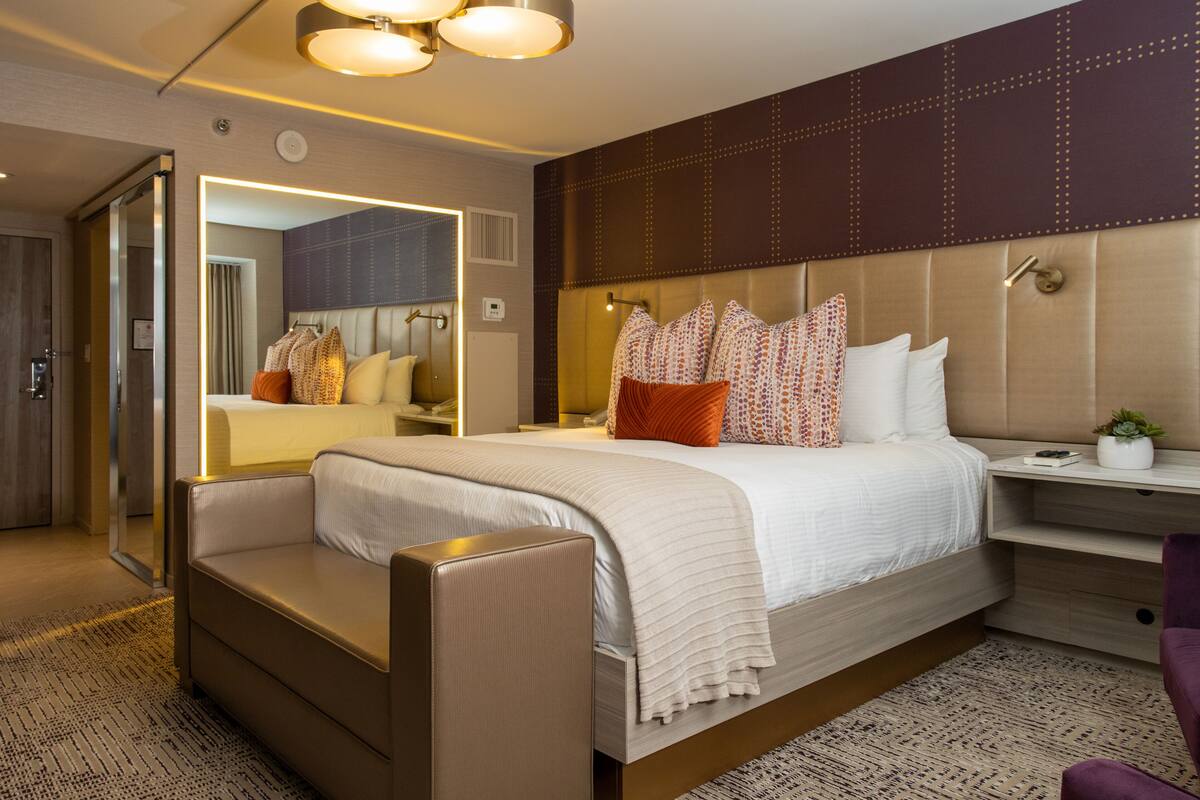 A modern hotel room with a large bed, a seating area, a vanity, and a mirror.