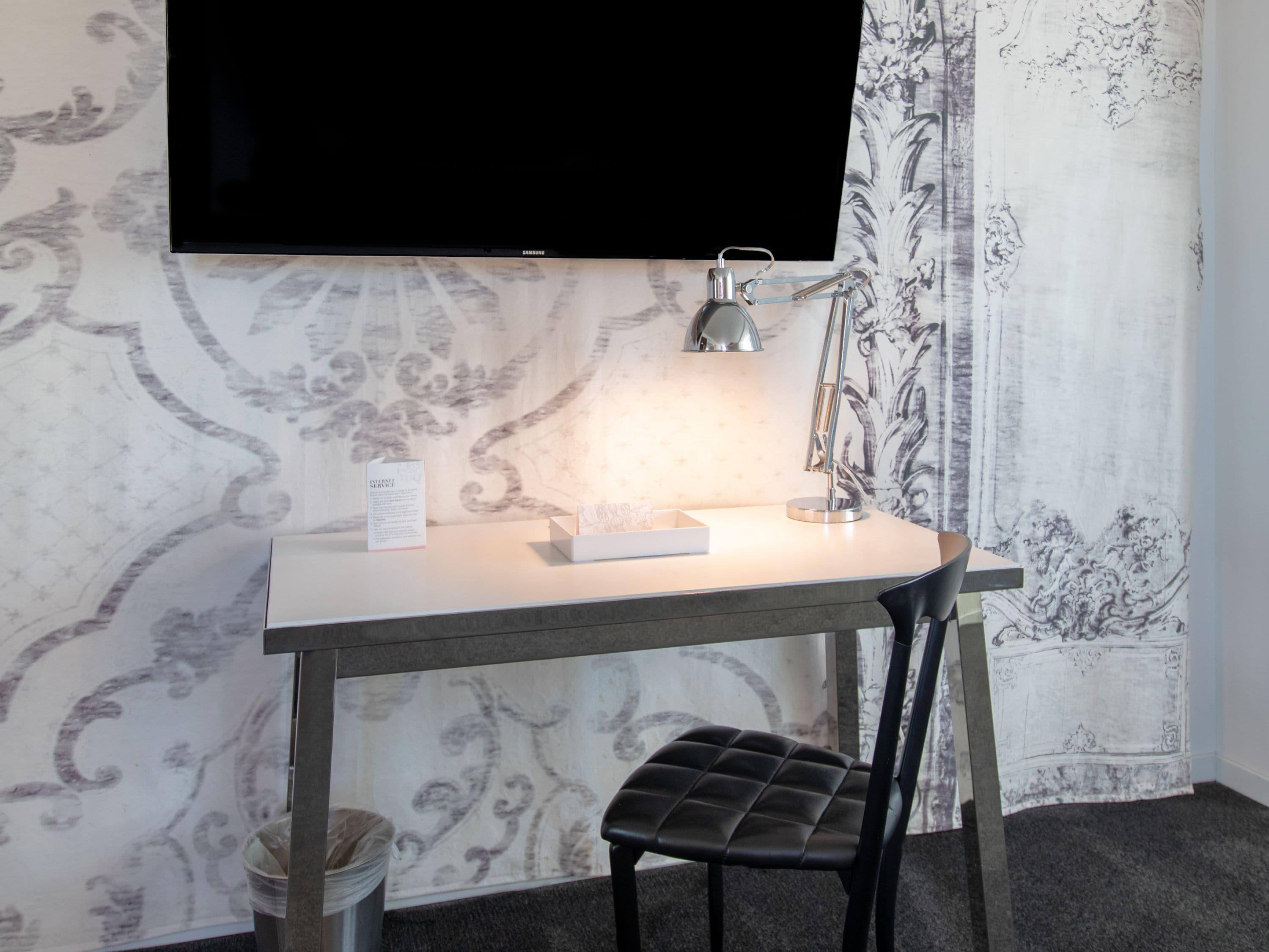 A hotel room with a desk, chair, and a flat-screen TV mounted on the wall.