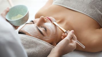 Une personne qui reçoit un soin du visage, avec un bol de crème et un pinceau.