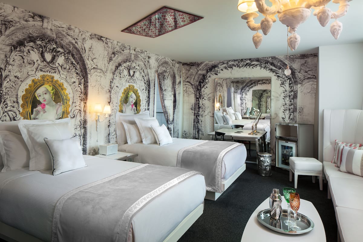 A hotel room with two beds, a dining area, and a bathroom.