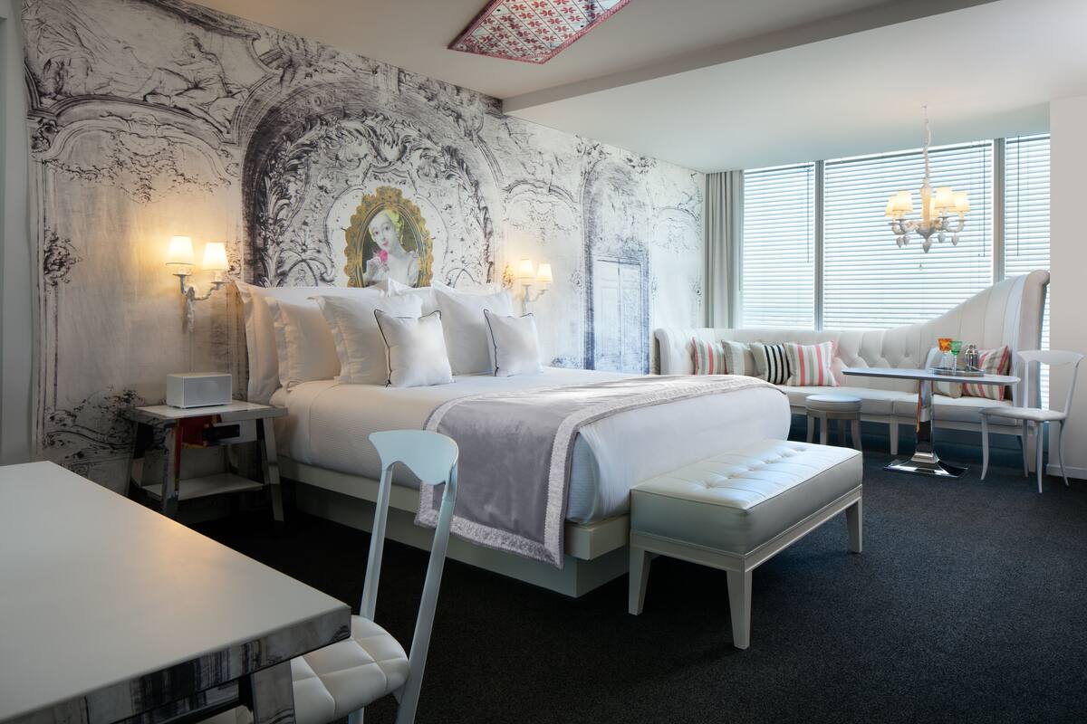A modern bedroom with a large bed, bedside tables, a desk, and a seating area with a sofa and chairs.