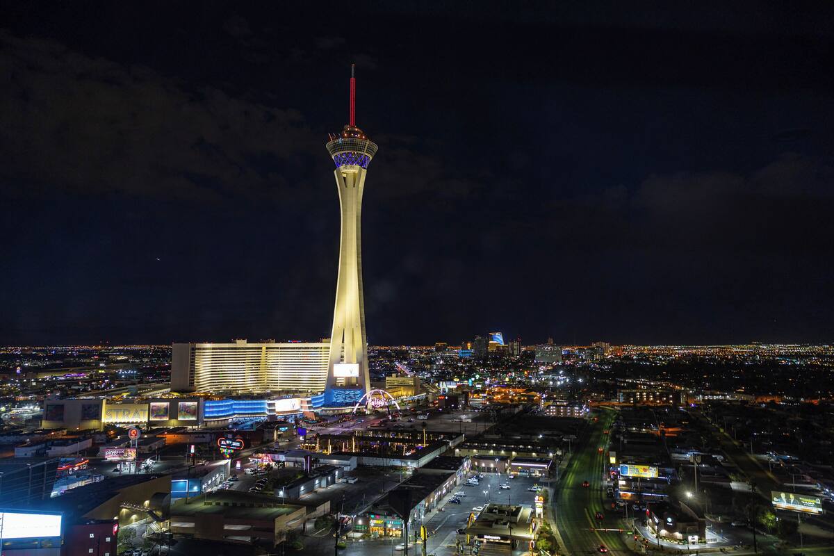A night view of a cityscape with a prominent tower and a casino complex.