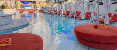 Zona de piscina con sillas de descanso rojas y toldos blancos.