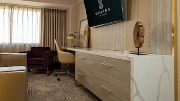 Ein Hotelzimmer mit einem großen Flachbildfernseher an der Wand, einem Schreibtisch mit Schubladen, einem Stuhl und einem Sofa.