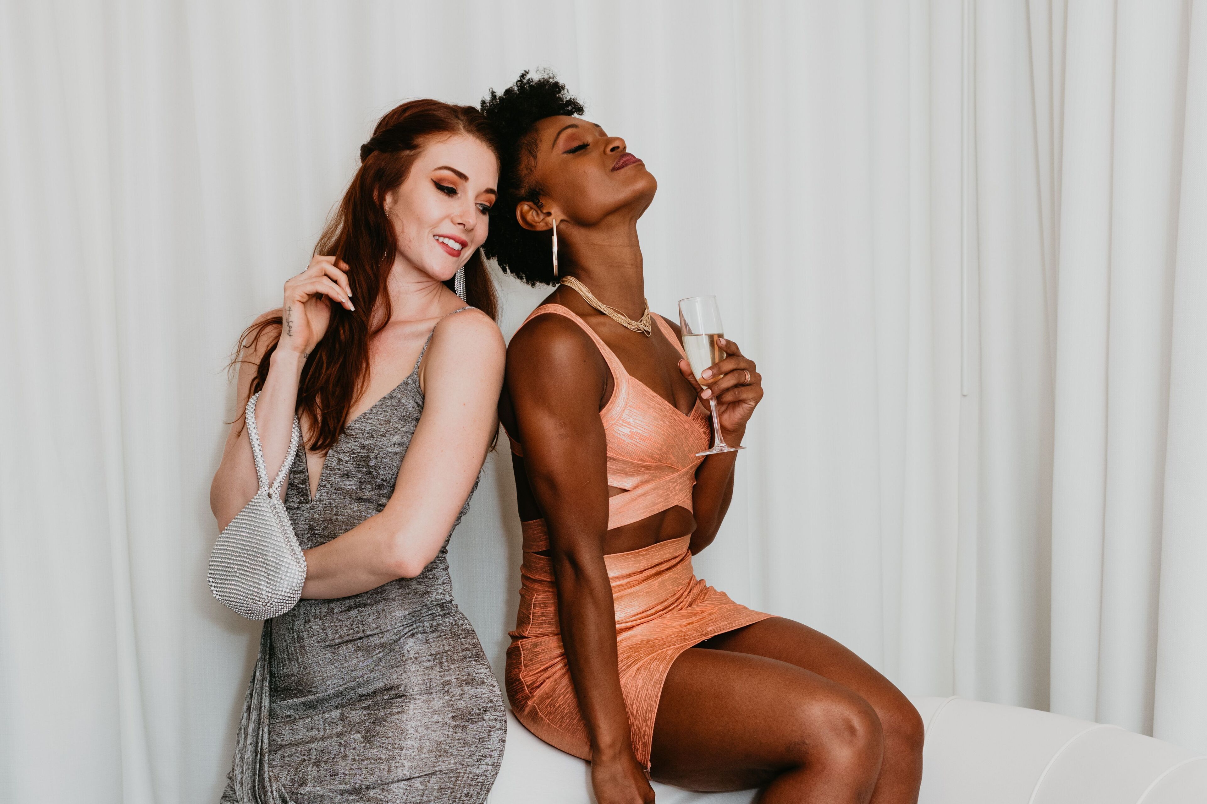 Two individuals seated on a white couch against a white curtain backdrop.