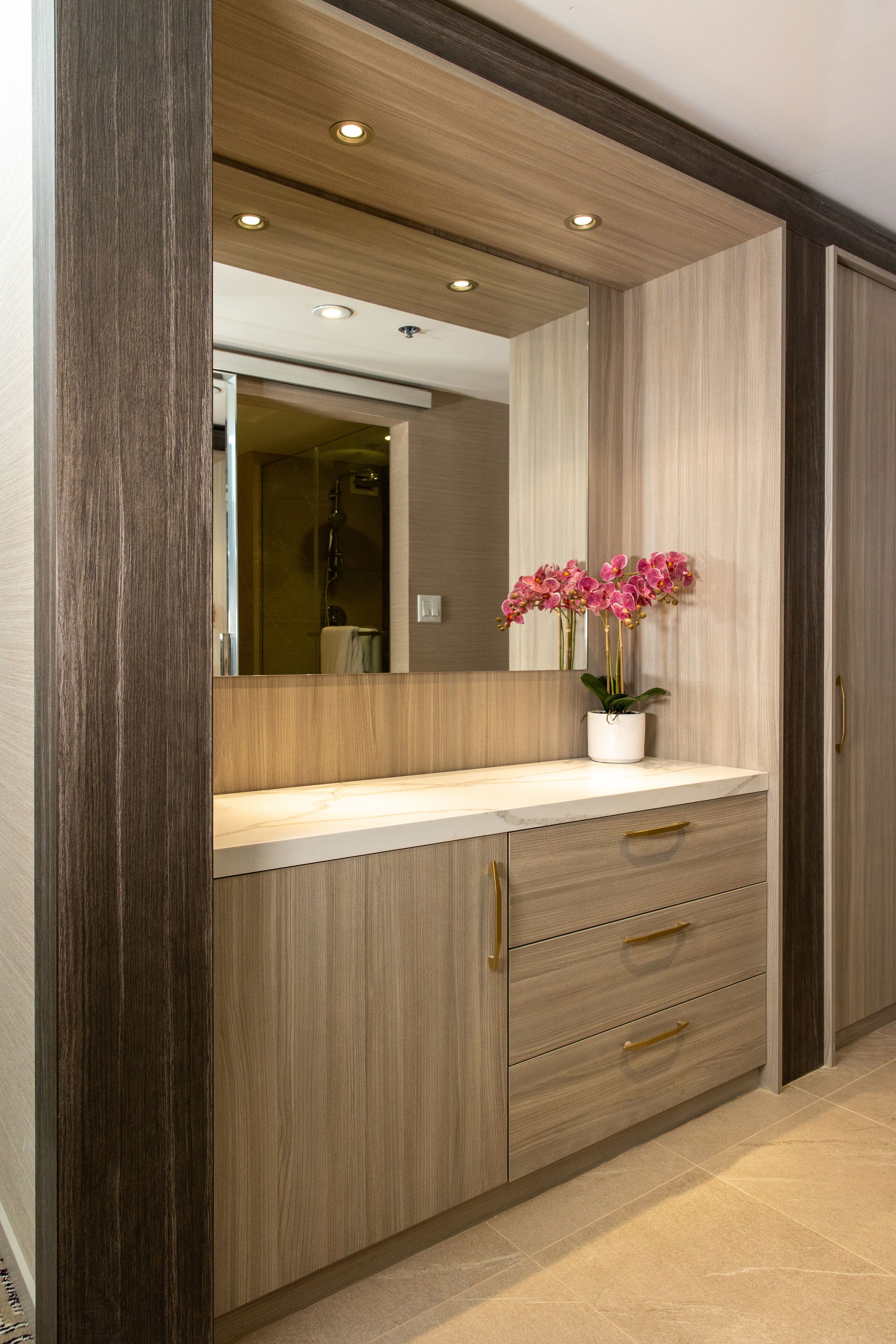 Een badkamer met een houten wastafelmeubel, een spiegel en een vaas met roze bloemen.