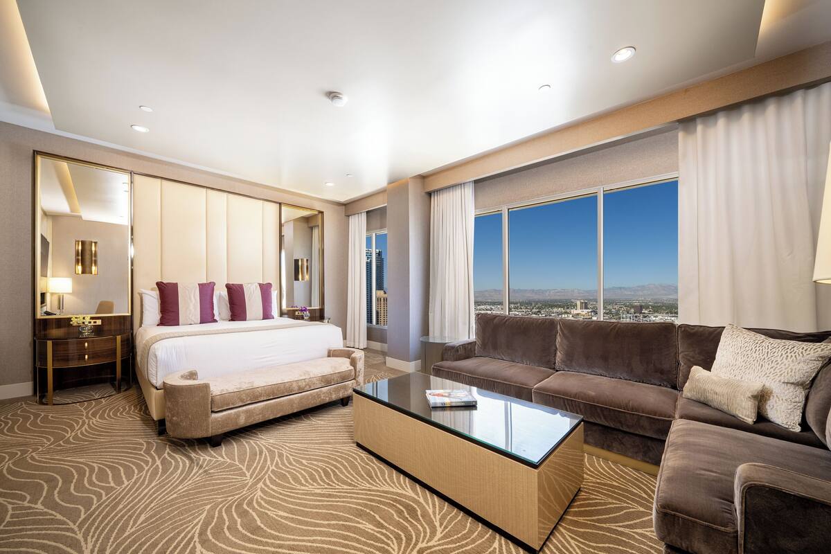 A hotel room with a large bed, a sofa, a coffee table, and a view of the city.