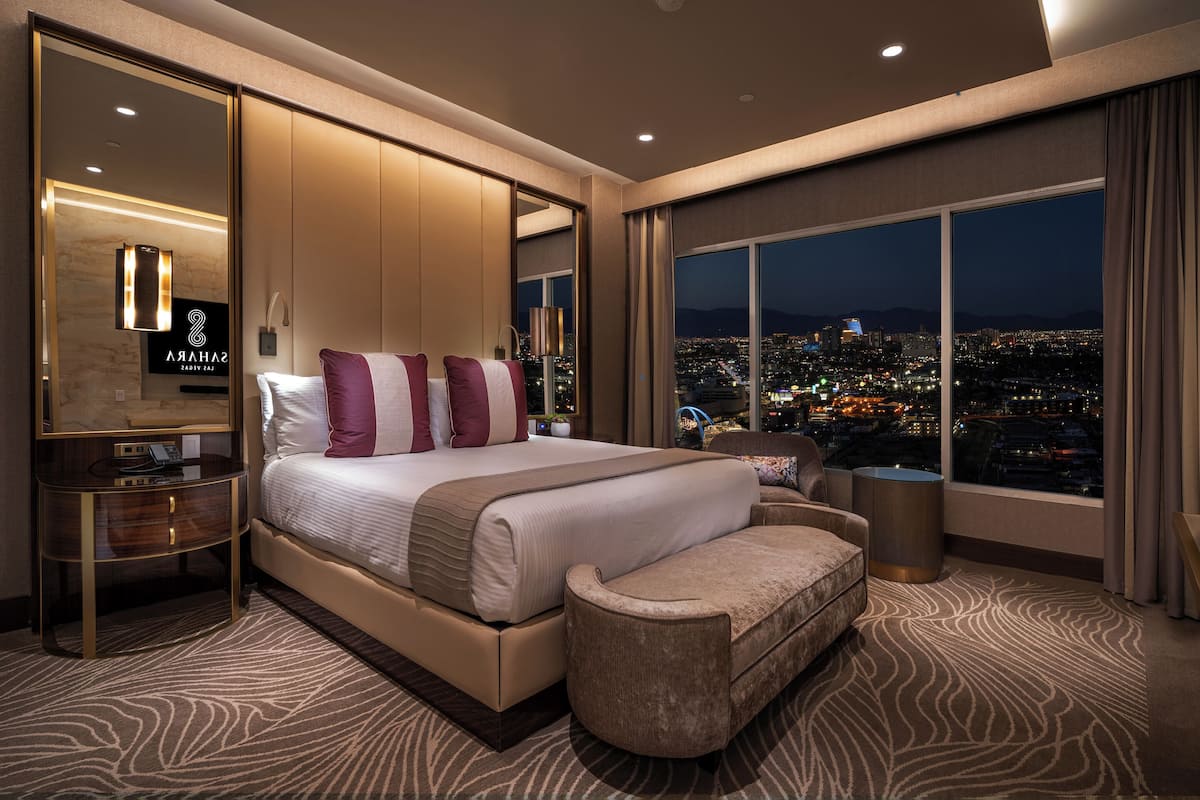 A modern hotel room with a large bed, a seating area, and a city view.