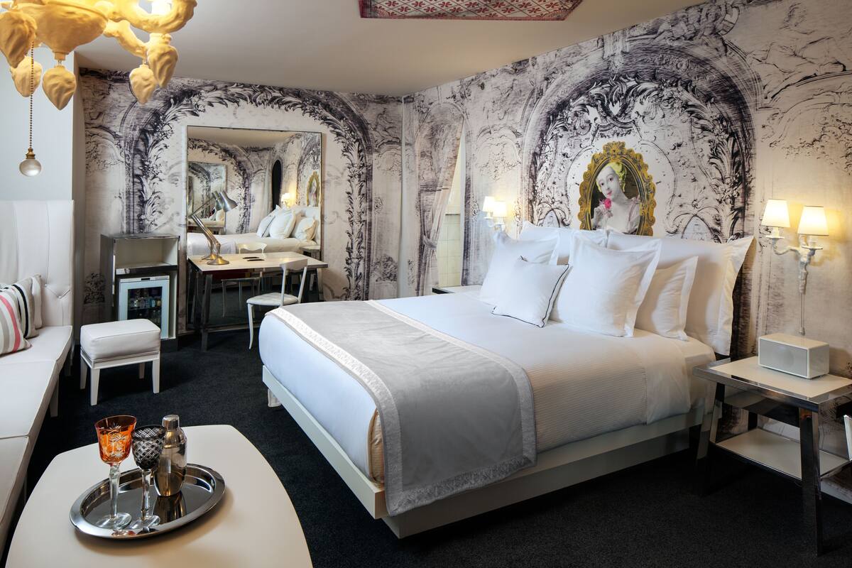 A hotel room with a large bed, a desk, a chair, and a tray with a glass and a bottle.