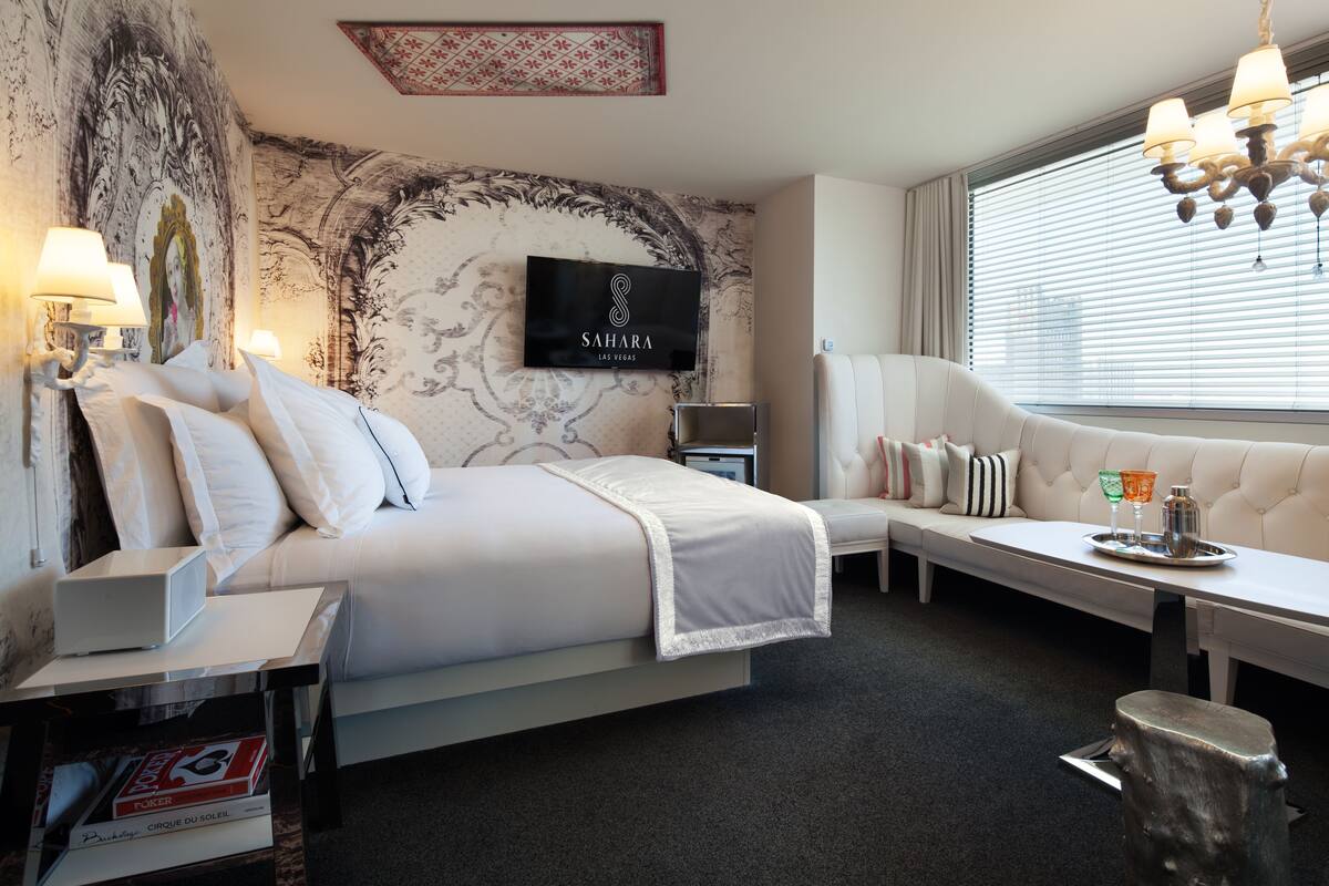 A hotel room with a bed, a sofa, a TV, and a window with blinds.