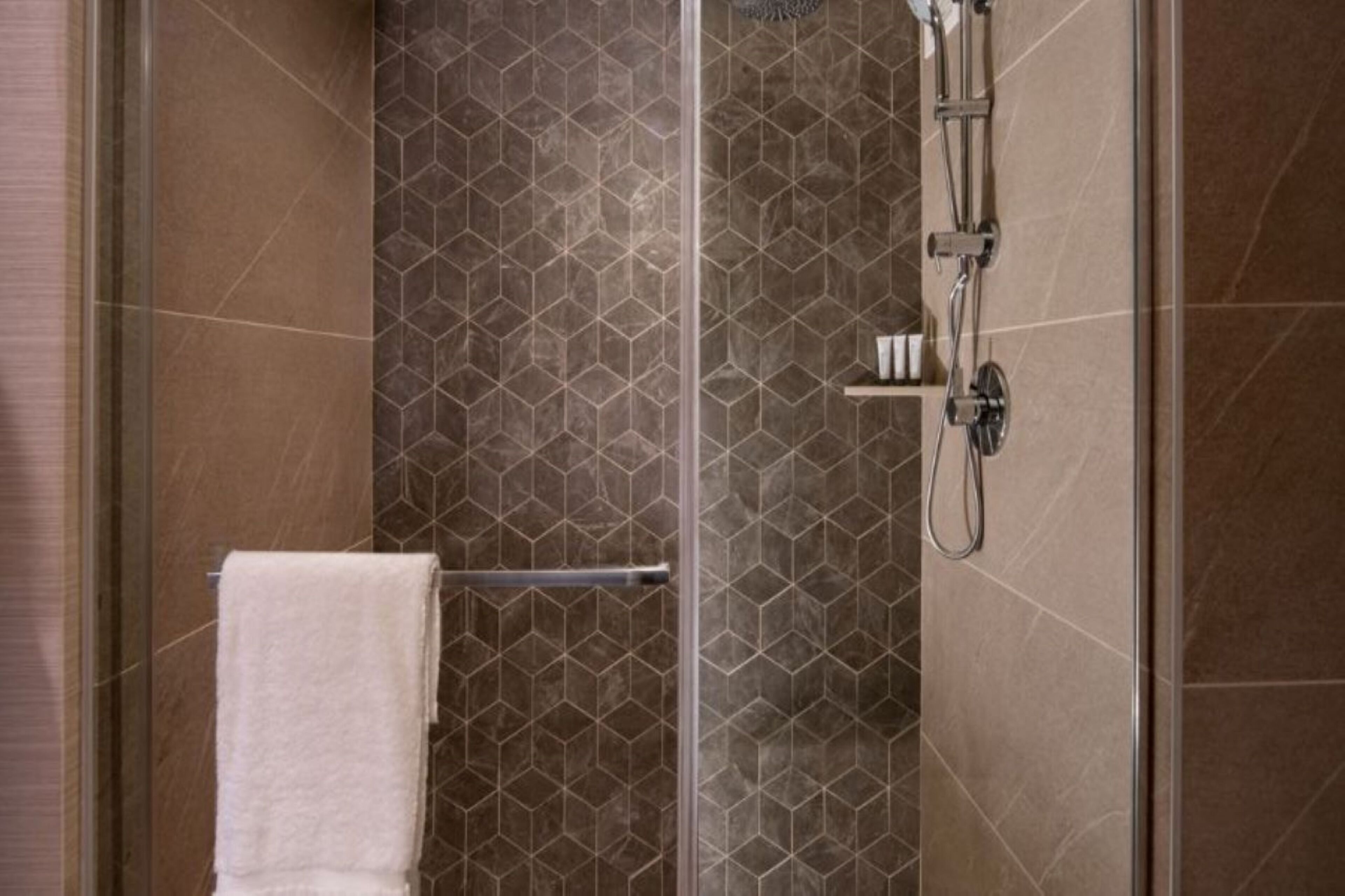 A shower with a glass door, a towel rack, and a shelf with toiletries.