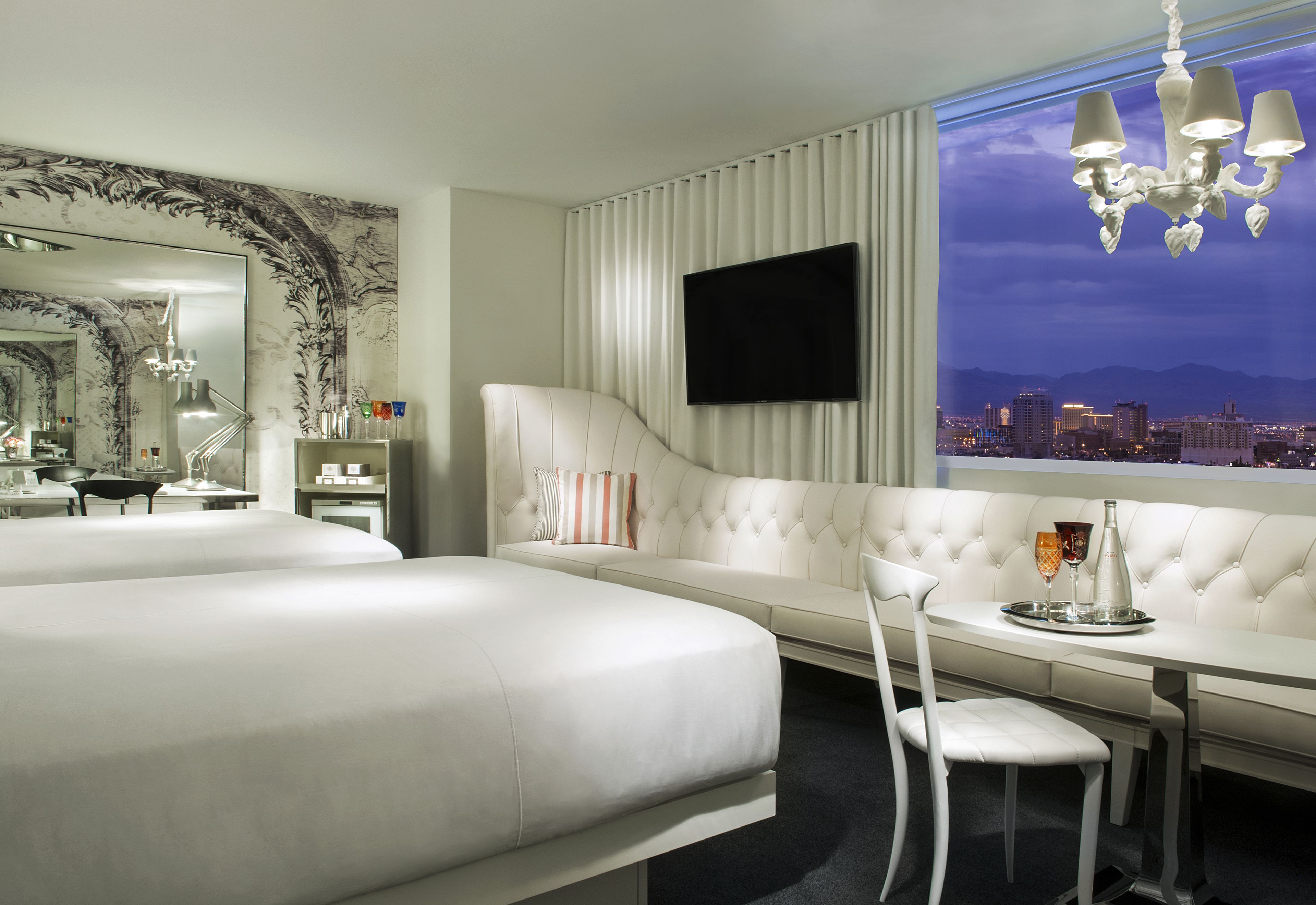 A hotel room with a large bed, a seating area with a TV, and a view of a cityscape at night.