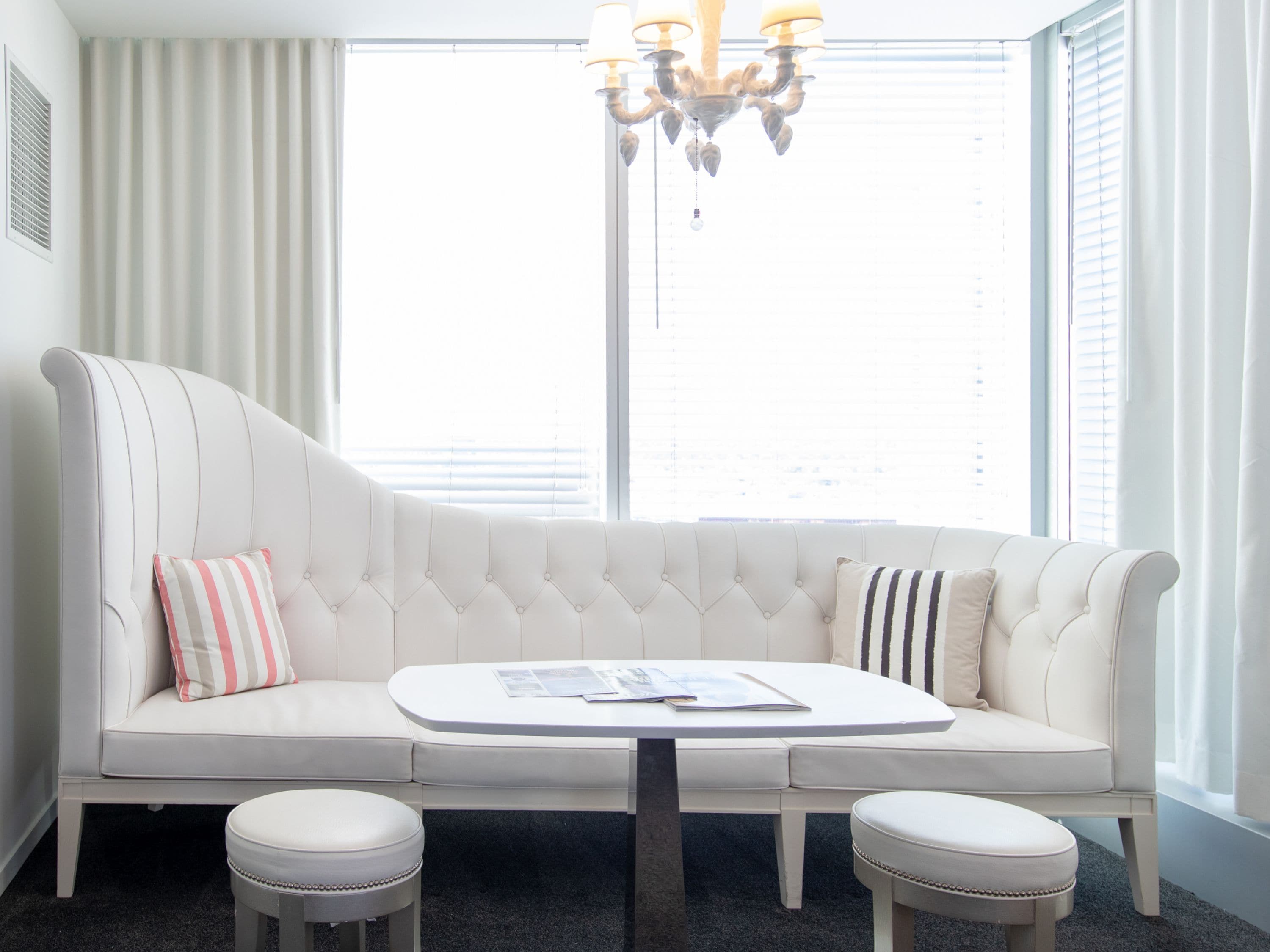 Uma sala de estar moderna com um sofá branco, dois pufes, uma mesa de centro redonda e um candelabro.