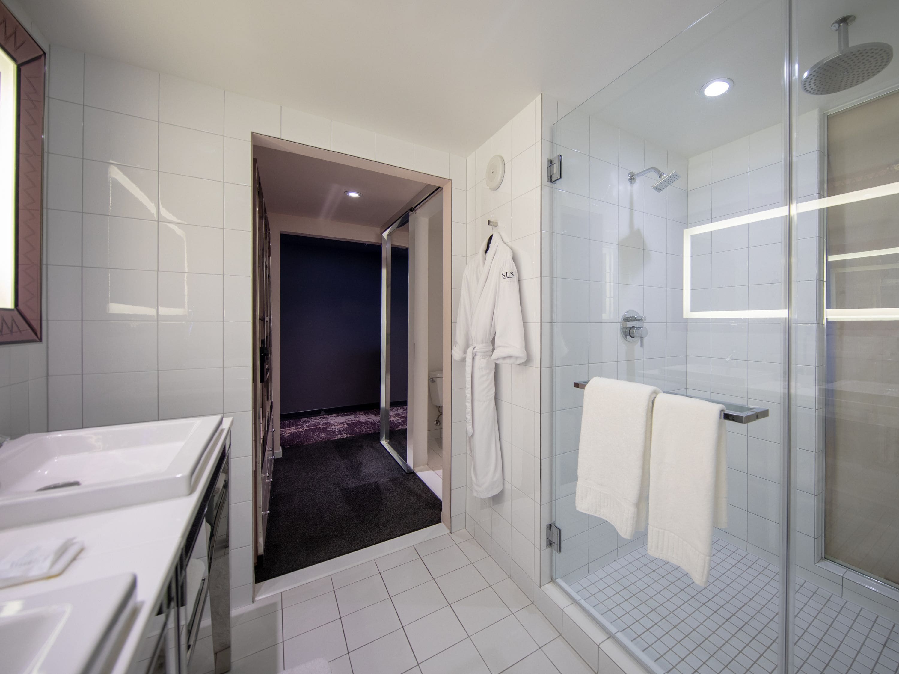 A modern bathroom with a glass shower enclosure, white tiled walls, and a dark-colored floor.