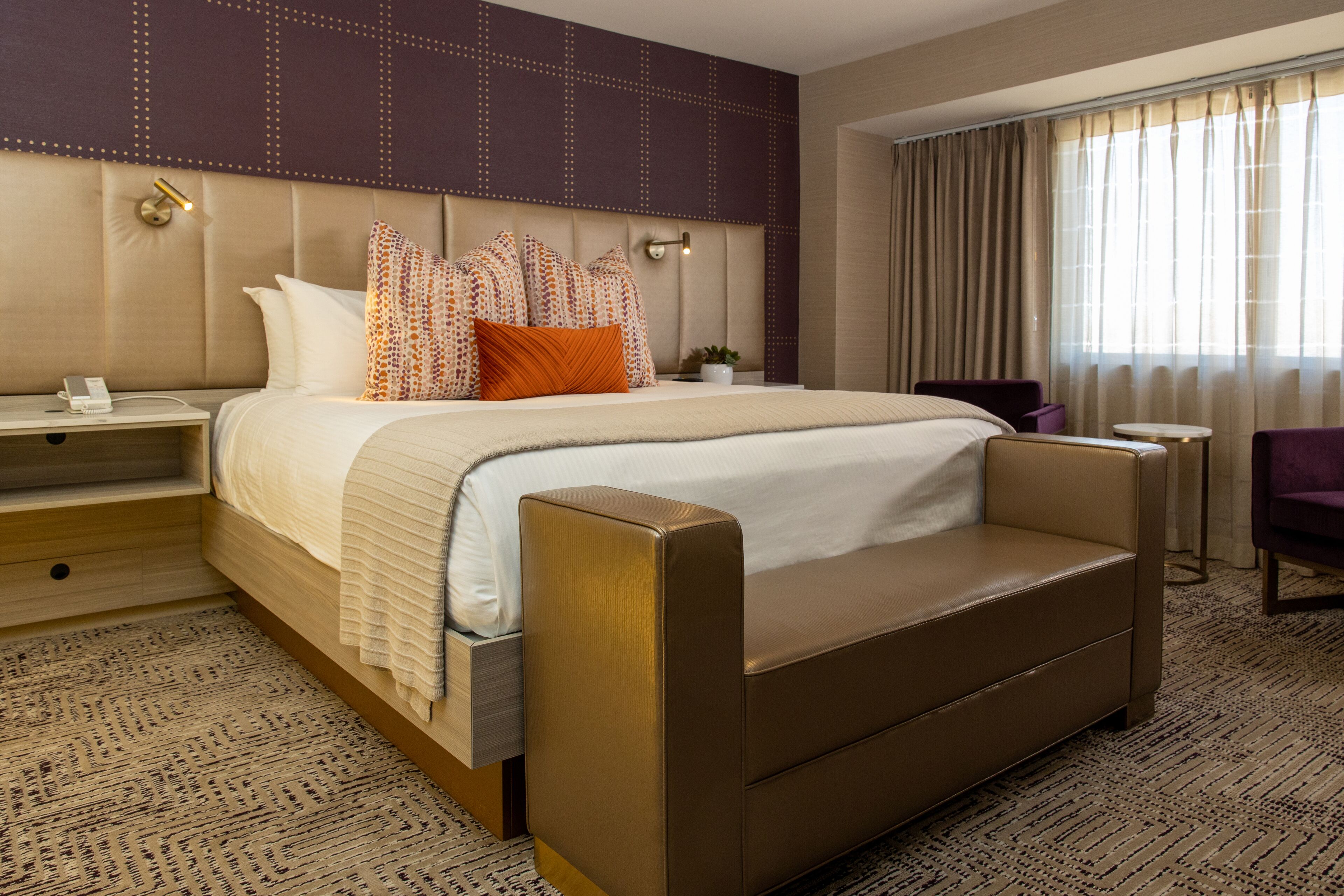 Een hotelkamer met een groot bed, een nachtkastje, een bureau, een stoel en een raam met gordijnen.