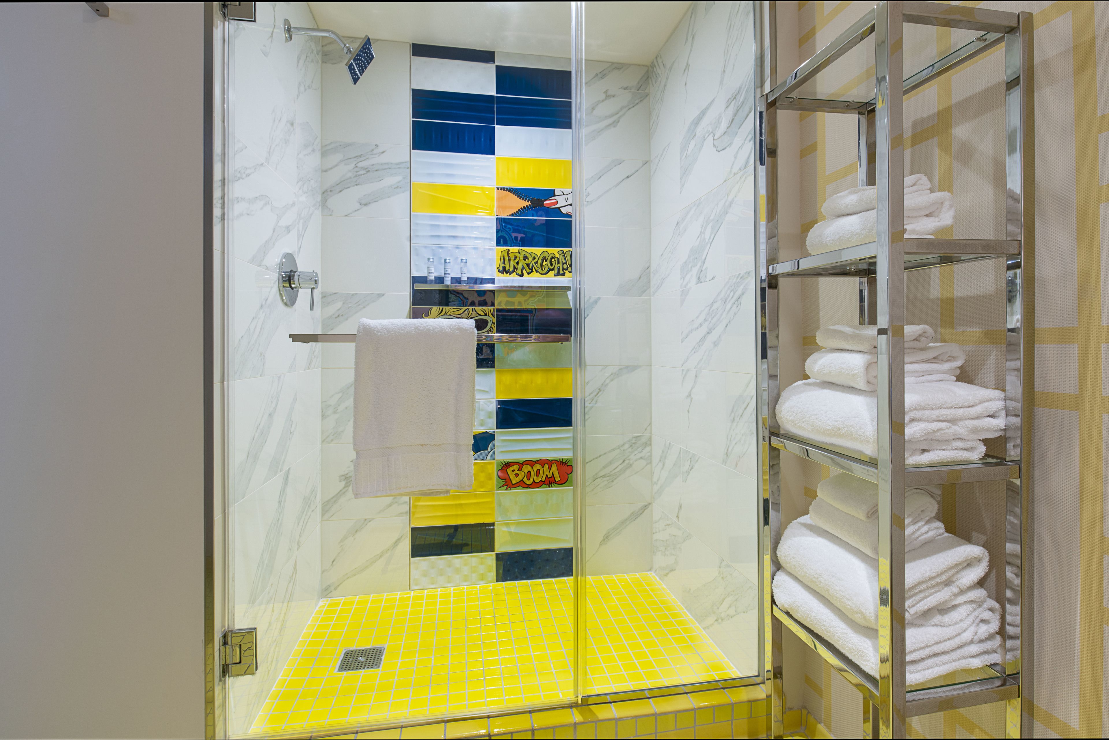 A bathroom with a glass shower enclosure, a yellow-tiled shower floor, and a towel rack with folded towels.