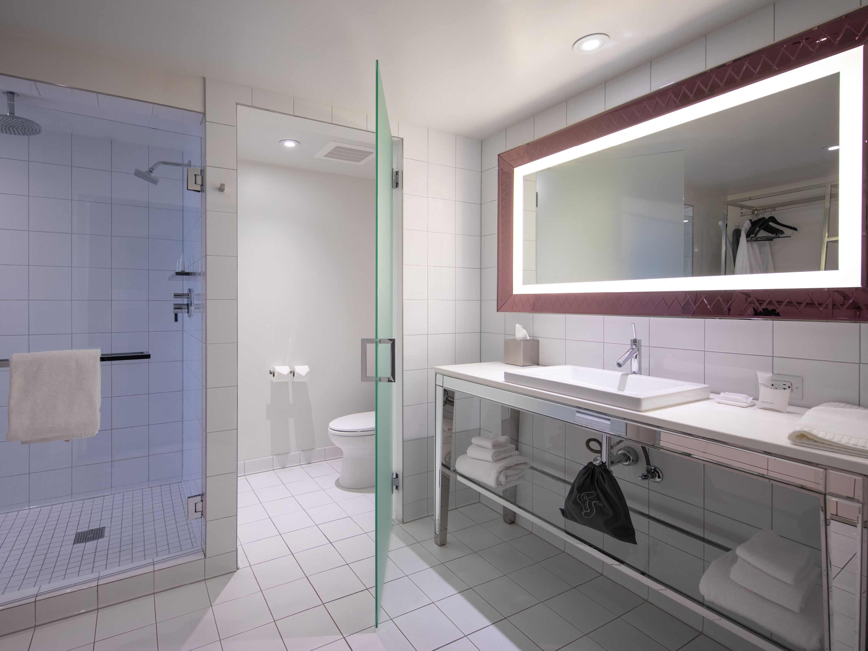 Une salle de bain moderne avec une douche à parois de verre, des toilettes blanches et un meuble-lavabo doté d’un grand miroir.