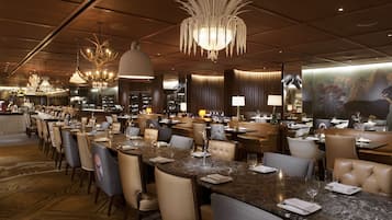 Un restaurante espacioso con varias mesas, candelabros elegantes y un ambiente cálido.