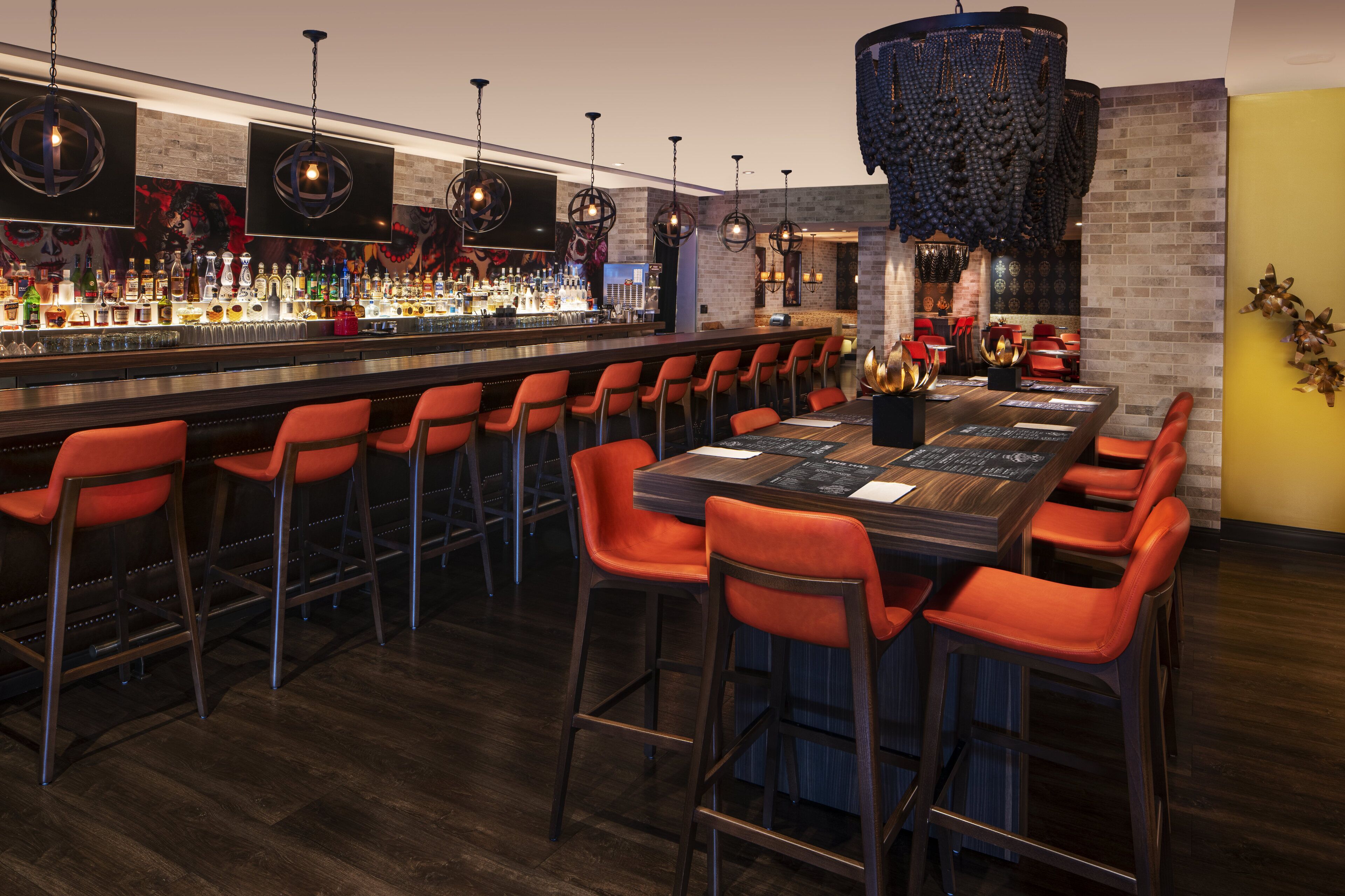 A bar area with multiple seating options, a long counter with a variety of bottles, and decorative lighting fixtures.