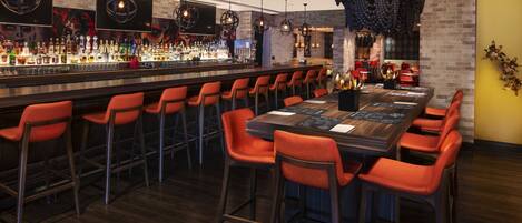 A bar area with multiple seating options, a long counter with a variety of bottles, and decorative lighting fixtures.