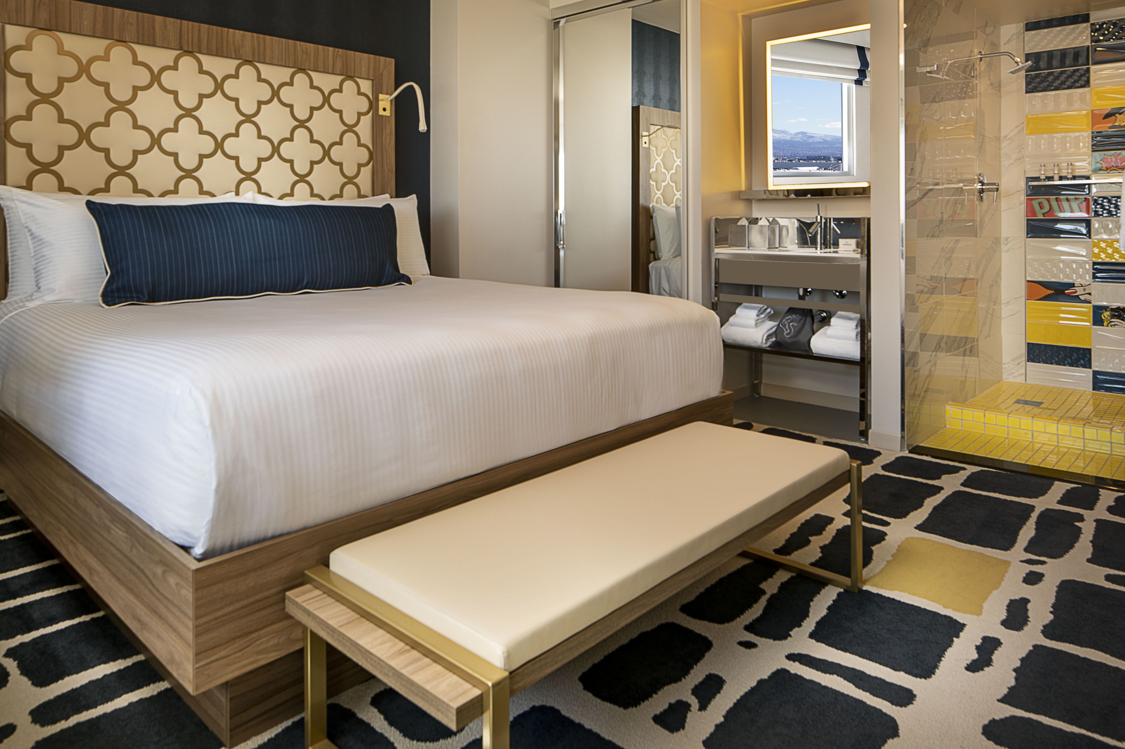 A hotel room with a large bed, a bench, a walk-in closet, and a shower area.