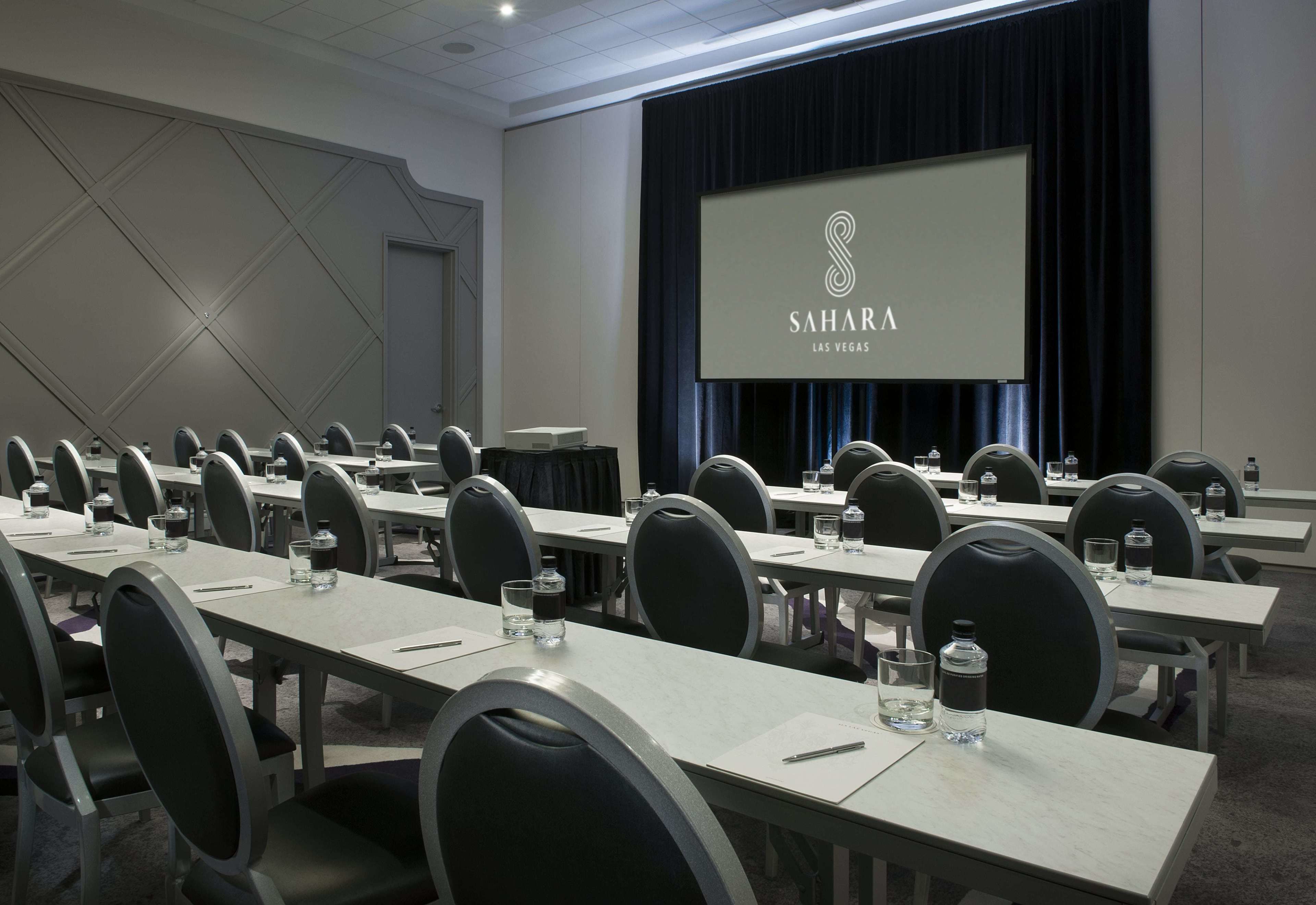 A conference room with multiple tables, chairs, and a large screen displaying "Sahara Las Vegas".