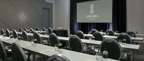 A conference room with multiple tables, chairs, and a large screen displaying "Sahara Las Vegas".