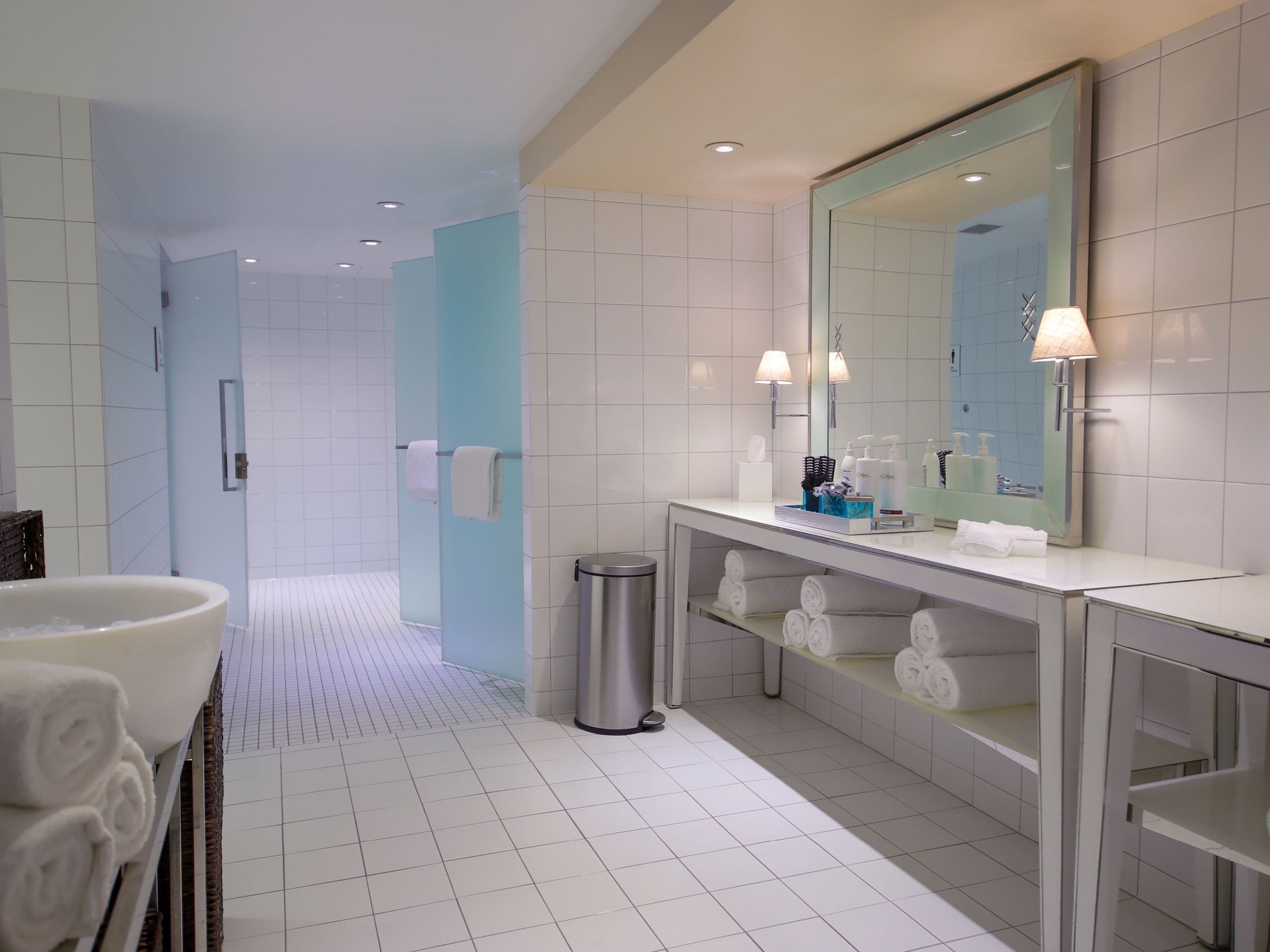 A modern bathroom with a large mirror, white tiles, a sink with a basin, and a shelf with toiletries.