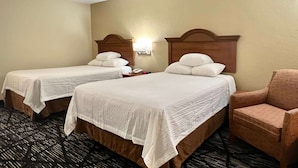 Habitación de hotel con dos camas individuales, una mesita de noche, una lámpara y una silla.