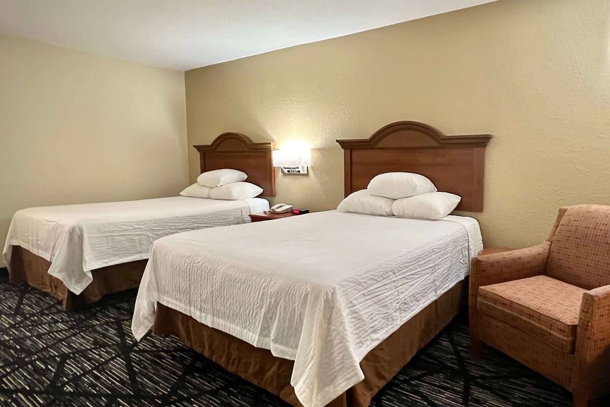 A hotel room with two single beds, a nightstand, a lamp, and a chair.