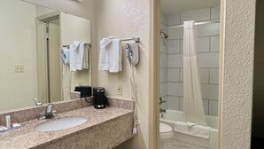 Un baño con encimera de granito, un lavabo, un espejo, un secador de pelo y una ducha con cortina.