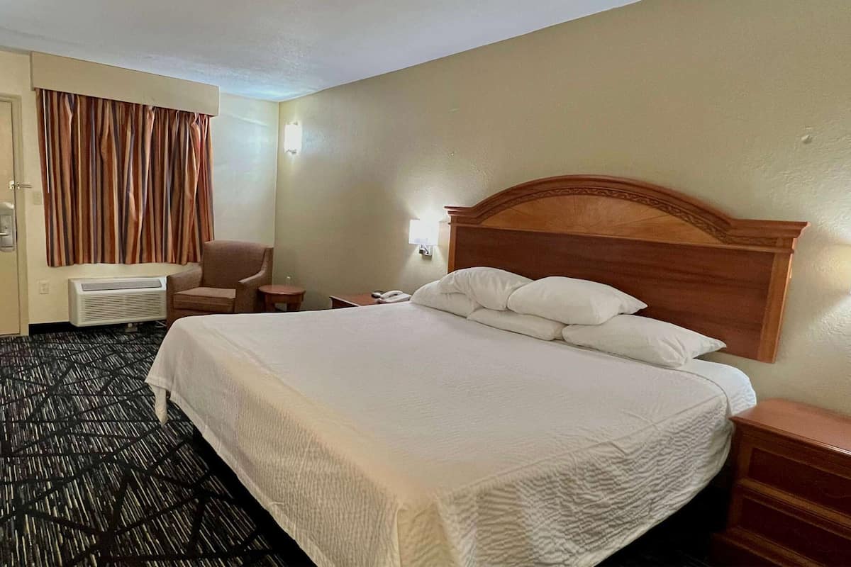 A hotel room with a large bed, a chair, a desk, and a telephone.