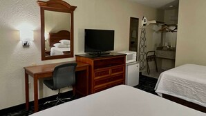 Habitación de hotel con cama, escritorio con silla, televisor, microondas, espejo y zona de ducha.