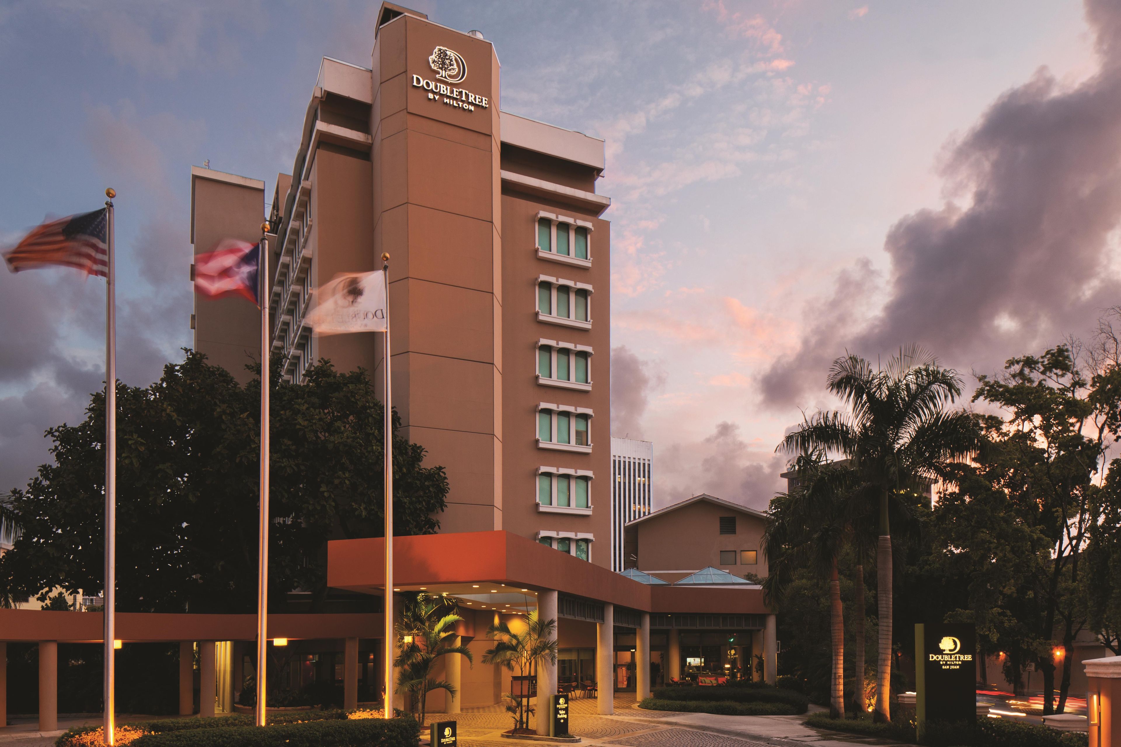Un hotel con un letrero llamativo, varias banderas y una entrada bien iluminada.