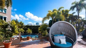 A poolside area with a wicker chair, potted plants, and a view of a building. - DoubleTree by Hilton San Juan (San Juan)