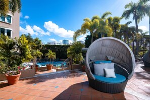A poolside area with a wicker chair, potted plants, and a view of a building. - DoubleTree by Hilton San Juan (San Juan)