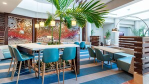 A modern lounge area with a large central table, blue chairs, and a decorative wall with mosaic tiles. - DoubleTree by Hilton San Juan (San Juan)