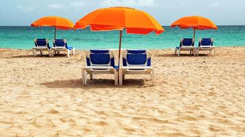 Una playa con hileras de sillas azules bajo sombrillas naranjas.