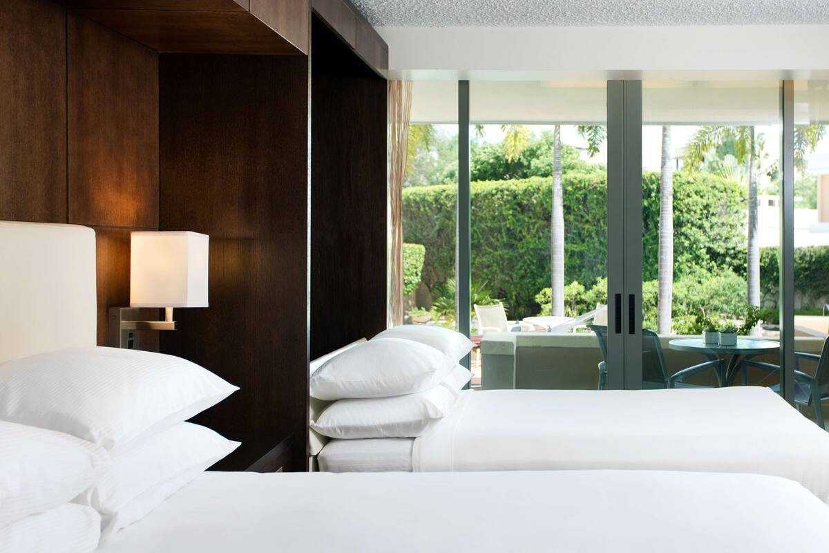 A hotel room with a large bed, a bedside lamp, and a view of a garden and outdoor seating area.