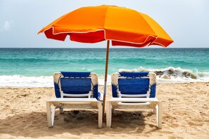 Dos sillas de playa con una sombrilla naranja.