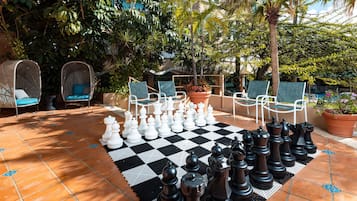 A chessboard set up outdoors with chairs and potted plants around.
